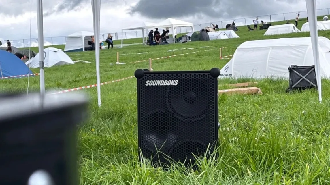 SOUNDBOKS-Lautsprecher steht im Gras vor Zelten auf einem Campingplatz als Lautsprecher für Festival mieten.