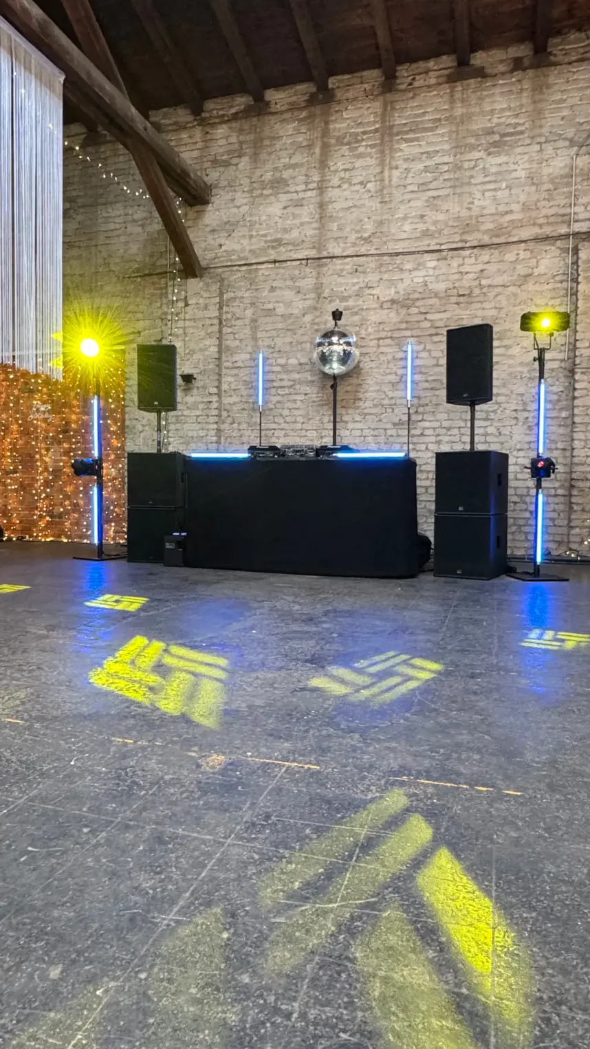 DJ-Pult mit zwei Lautsprechern auf Stativen, Diskokugel und Uplights in einer Scheune als PA-Anlage für Firmenevent mieten.