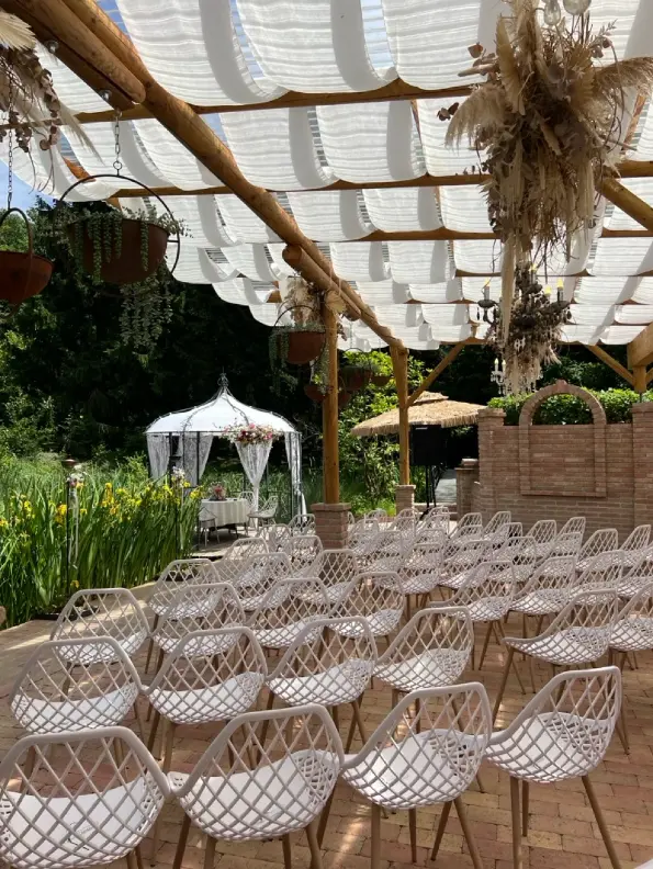 Weiße Stuhlreihen unter einer Pergola vor einem geschmückten Pavillon bei einer Gartenhochzeit als Veranstaltungstechnik für Hochzeit mieten.