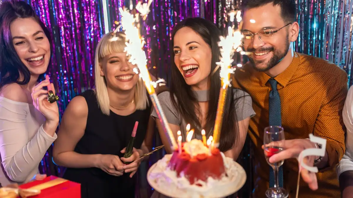 Freunde feiern einen runden Geburtstag mit Torte, Wunderkerzen und Sekt
