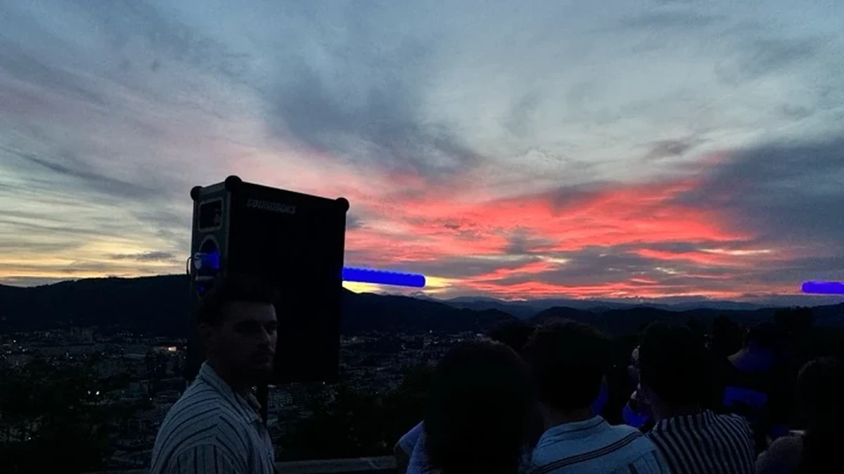 Feiernde auf einer überdachten Dachterrasse, während die Sonne hinter den Bergen untergeht