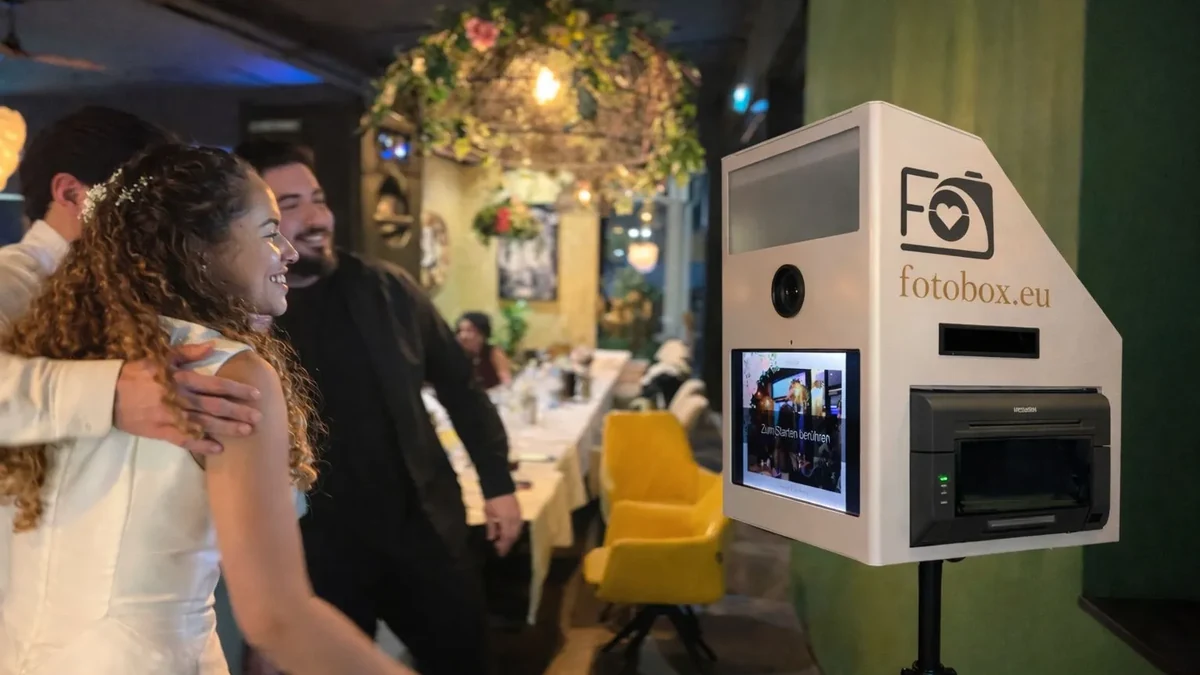 Hochzeitsgaeste posieren lachend vor einer Fotobox als Unterhaltung waehrend der Feier