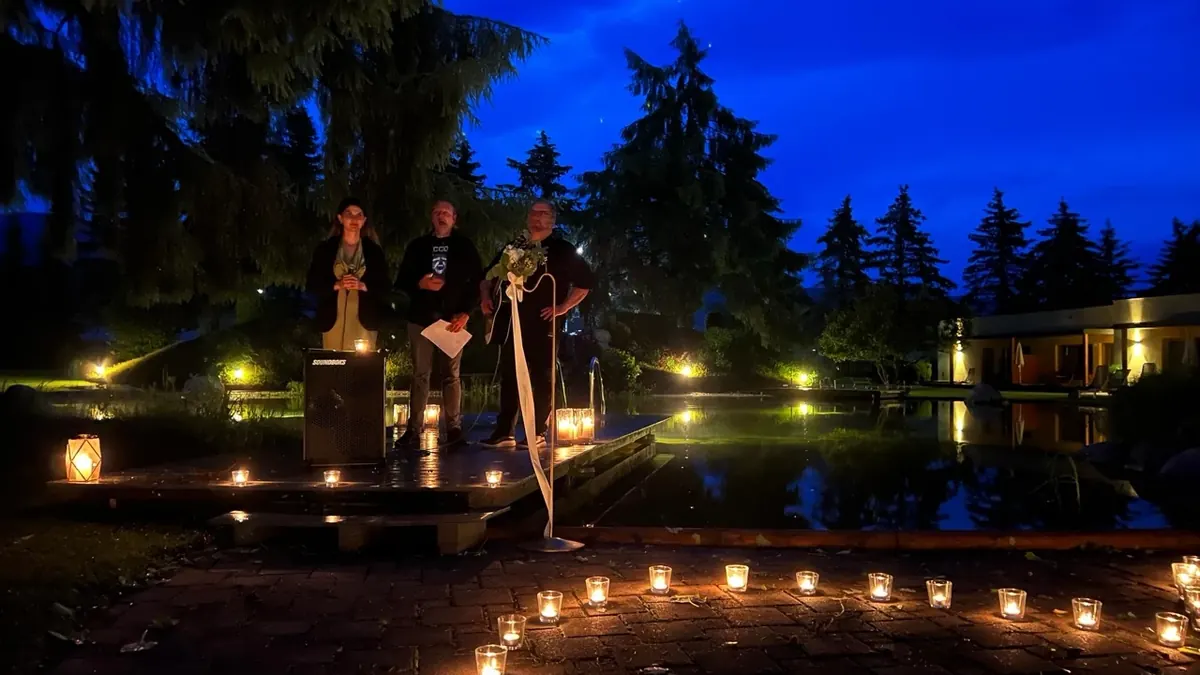 Abendliche freie Trauung an einem Teich mit vielen Kerzen, das Paar steht mit dem Redner am Mikrofon