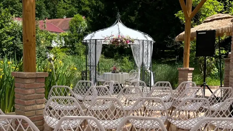 Reihen weisser Stuehle unter einer Pergola vor einem Pavillon mit Blumenschmuck