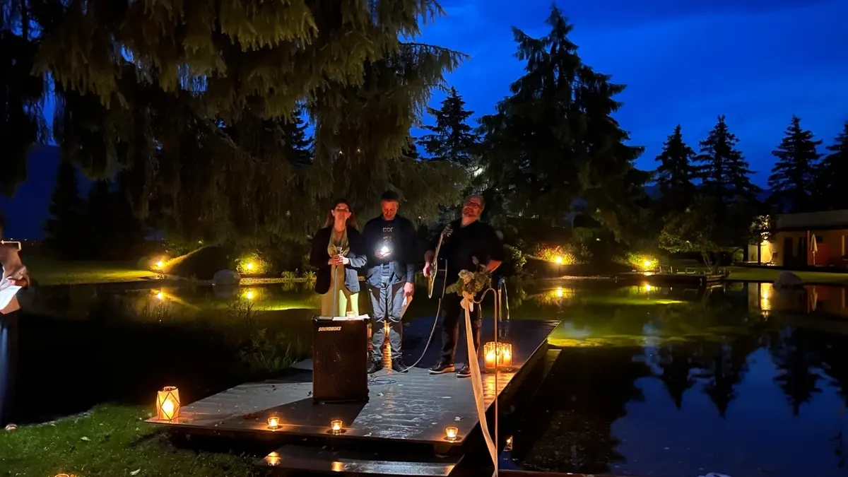 Drei Musiker spielen bei Nacht auf einem Holzsteg am Teich, ringsum brennen Kerzen
