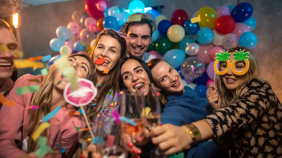 Kolleginnen und Kollegen stossen bei einer Weihnachtsfeier mit Sekt vor einer Ballonwand an