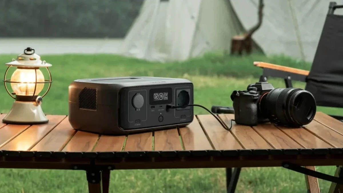 Powerstation lädt eine Kamera auf einem Campingtisch, dahinter Zelte auf dem Festivalgelände