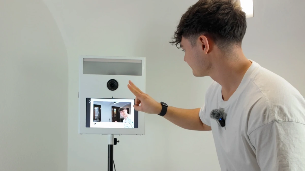 Ein junger Mann bedient den Touchscreen einer modernen, weißen Fotobox, die auf einem Stativ in einem hellen Raum steht.