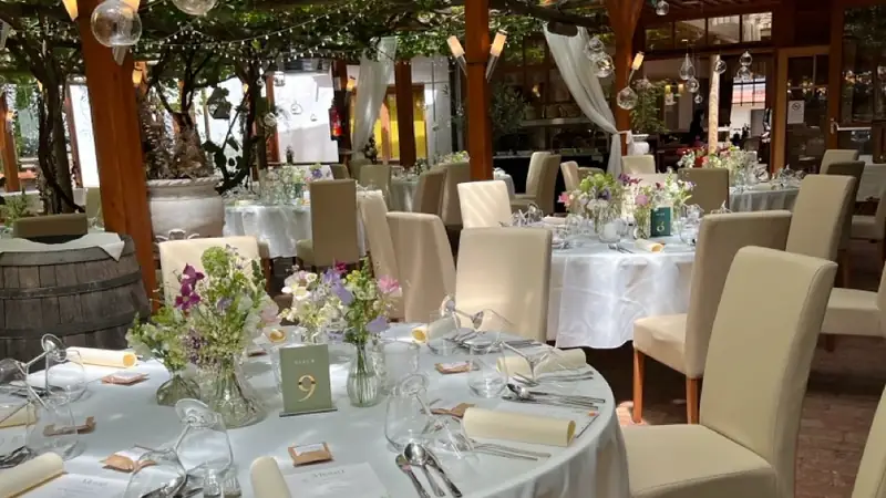 Gedeckte runde Tische mit Wildblumen unter einer Pergola beim Hochzeitsempfang am Nachmittag
