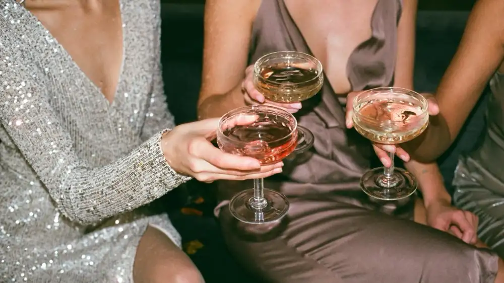 Drei Frauen in Abendkleidern stoßen bei einem runden Geburtstag mit Cocktails an