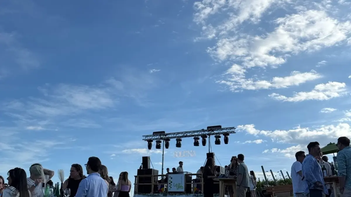 Gäste an Stehtischen auf einer Wiese bei einem Open-Air-Event mit Bühne im Hintergrund