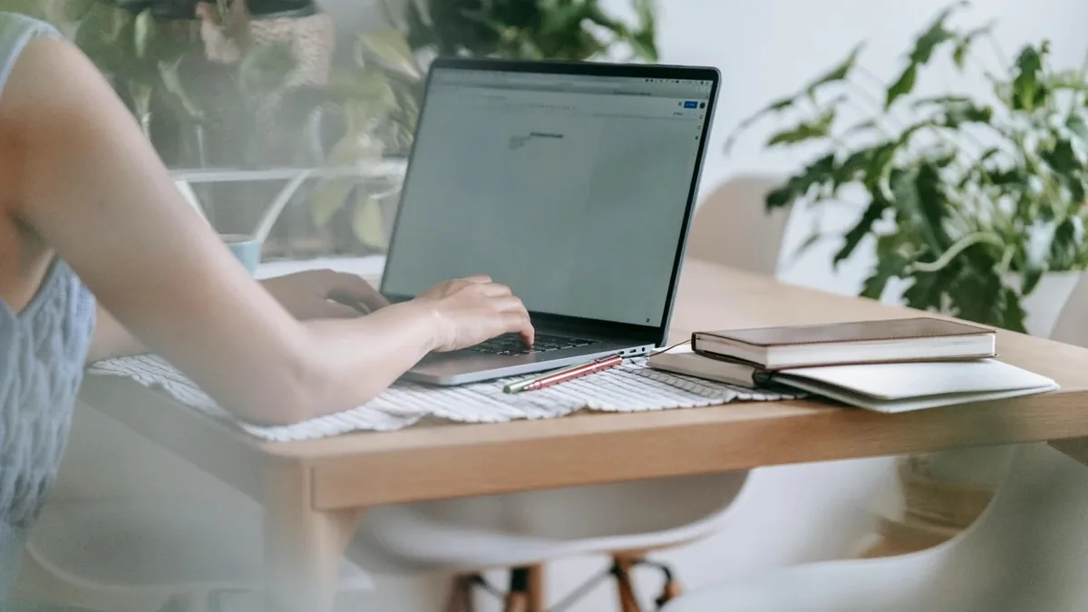 Frau arbeitet am Laptop an der Maturazeitung, daneben Notizbücher und Pflanzen