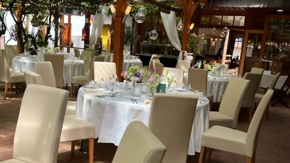 Festsaal unter Weinlaub mit runden weiß gedeckten Tischen und cremefarbenen Polsterstühlen