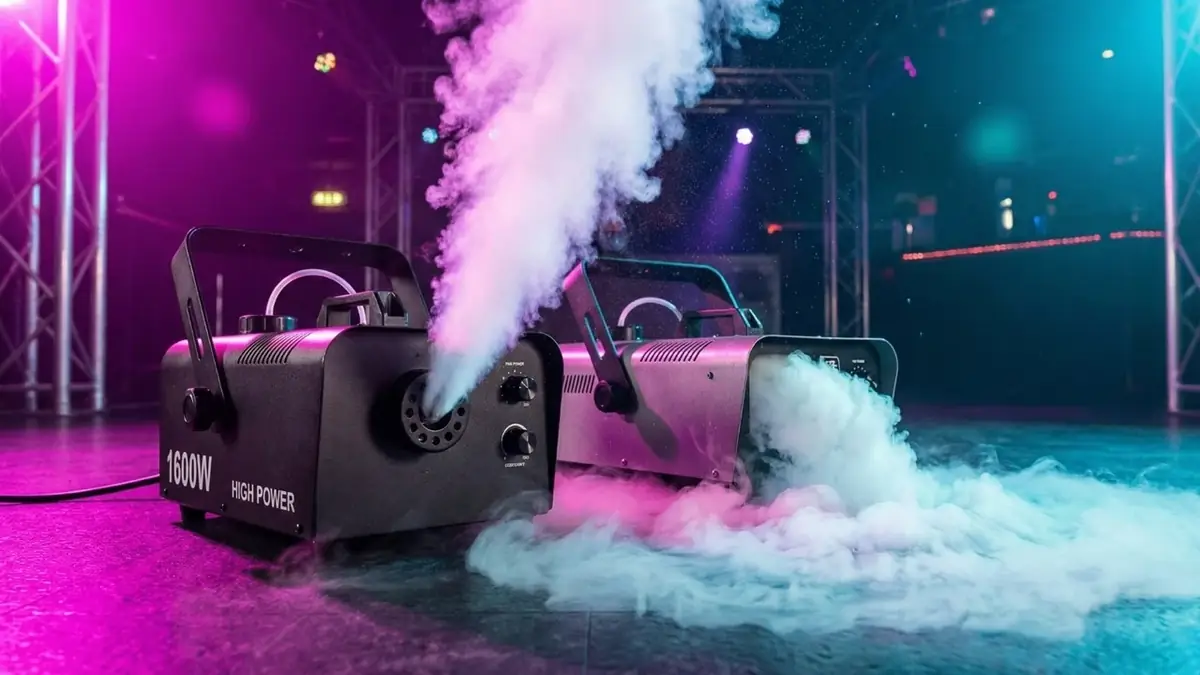 Zwei Nebelmaschinen stoßen dichten Nebel auf einer Bühne aus, beleuchtet in Pink und Blau
