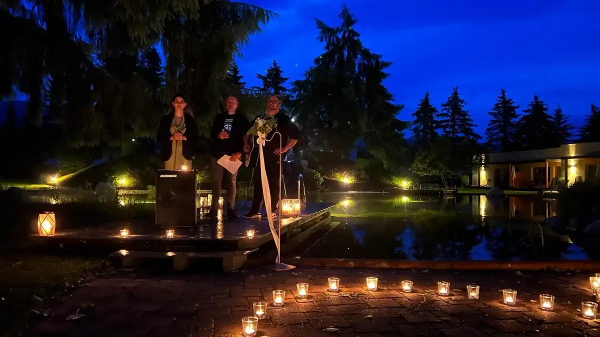 Abendveranstaltung an einem Teich mit Kerzen auf dem Boden und Gästen auf einem Holzsteg