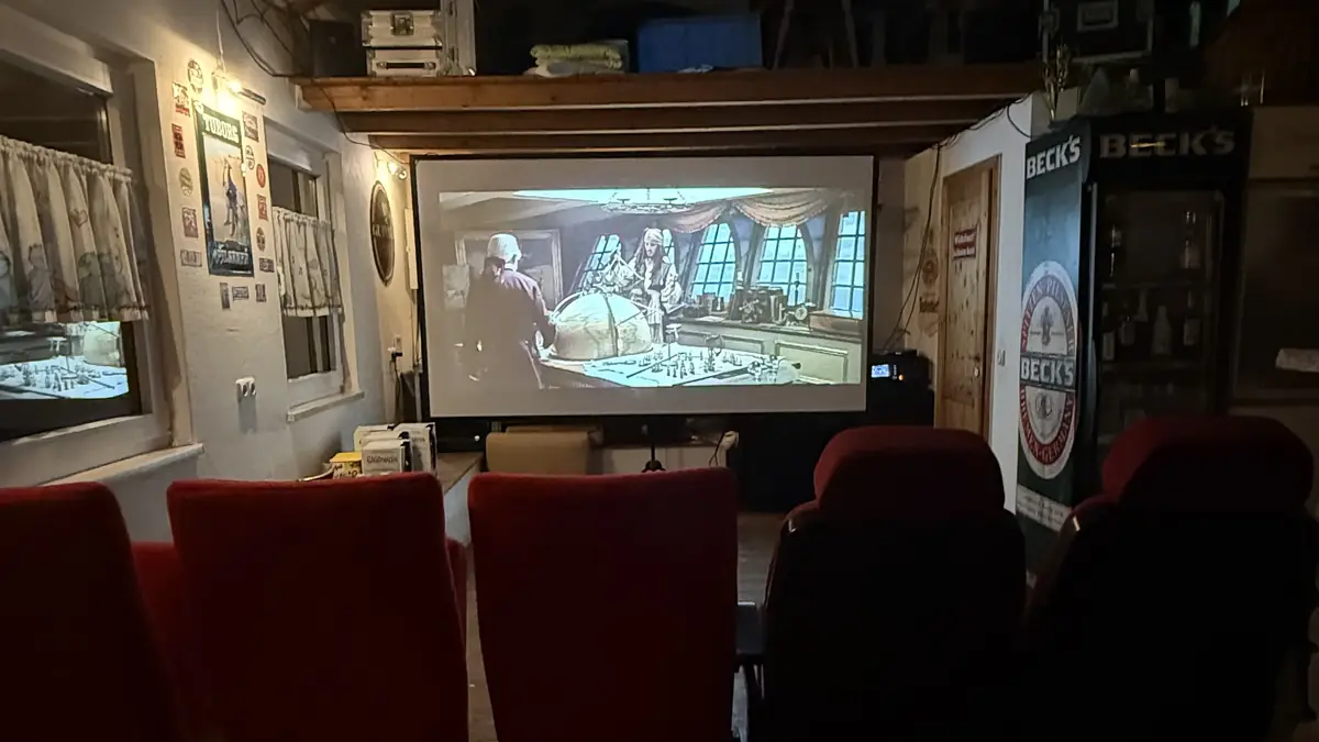 Filmvorführung mit Beamer und Leinwand in einem Partyraum mit roten Sitzgelegenheiten