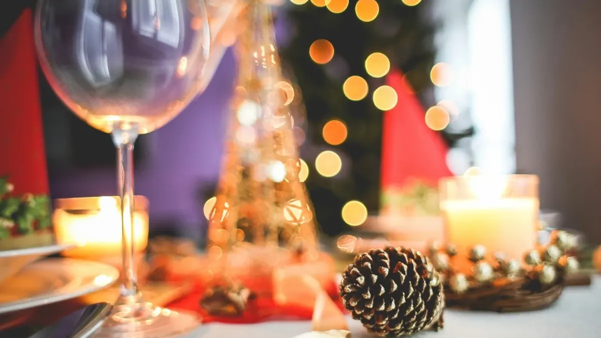 Weihnachtlich gedeckter Tisch mit Weinglas, Kerzen und Tannenzapfen vor unscharfen Lichtern