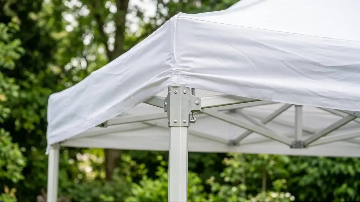 Nahaufnahme der Dachecke eines weißen Faltpavillons mit Aluminiumgestänge im Garten