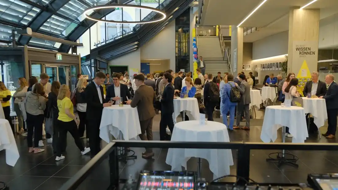 Blick über ein DJ-Pult auf Gäste an weiß gedeckten Stehtischen bei einem Event