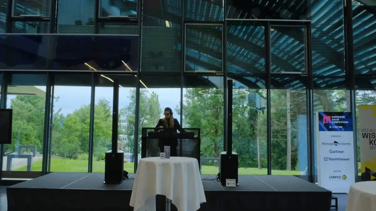 Weiter Blick in ein verglastes Foyer mit DJ auf der Bühne und Stehtischen davor