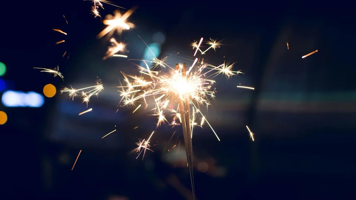 Funkelnde Wunderkerze sprüht Funken vor dunklem Hintergrund mit farbigen Lichtern