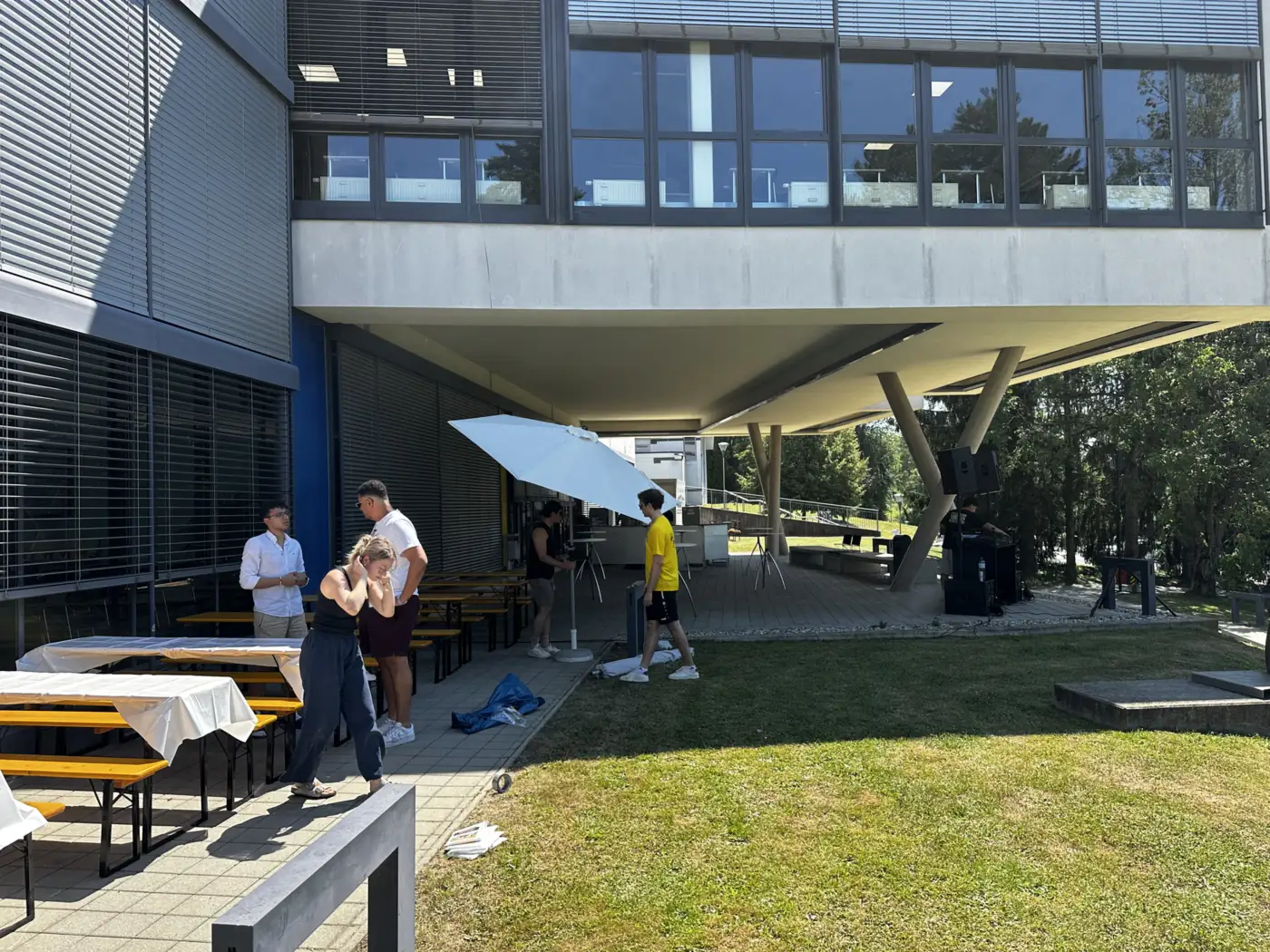 Helfer decken Biertische ein, daneben Sonnenschirm und Lautsprecher, wie bei einem Vereinsfest im Freien