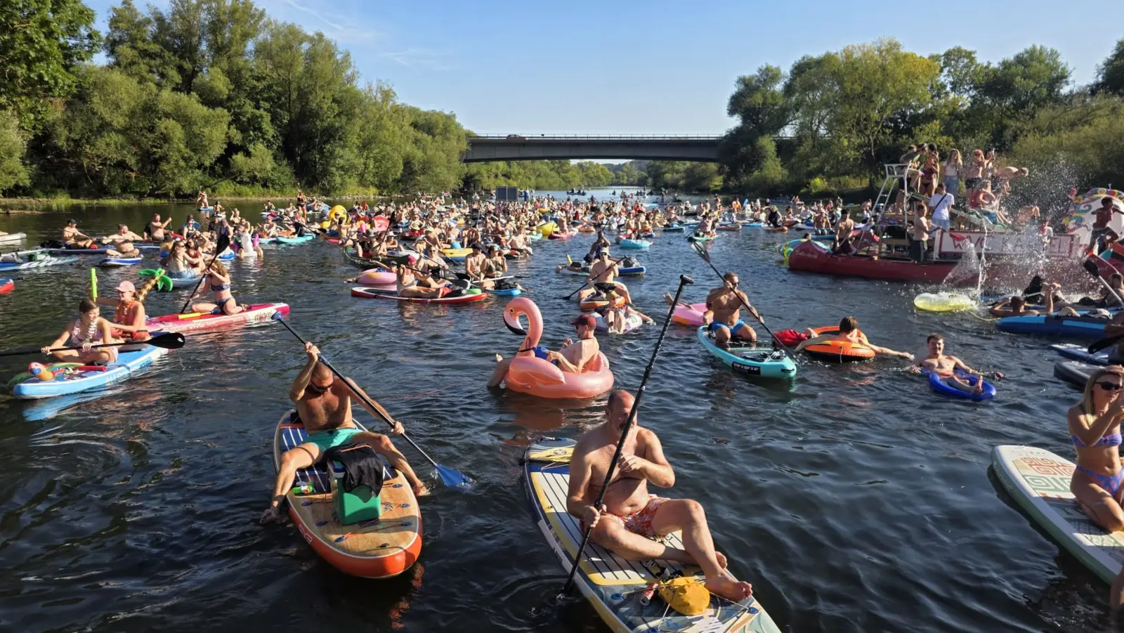 Floßrave auf der Fulda in Kassel: Hunderte Teilnehmer auf SUP-Boards und Luftmatratzen treiben unter einer Brücke flussabwärts