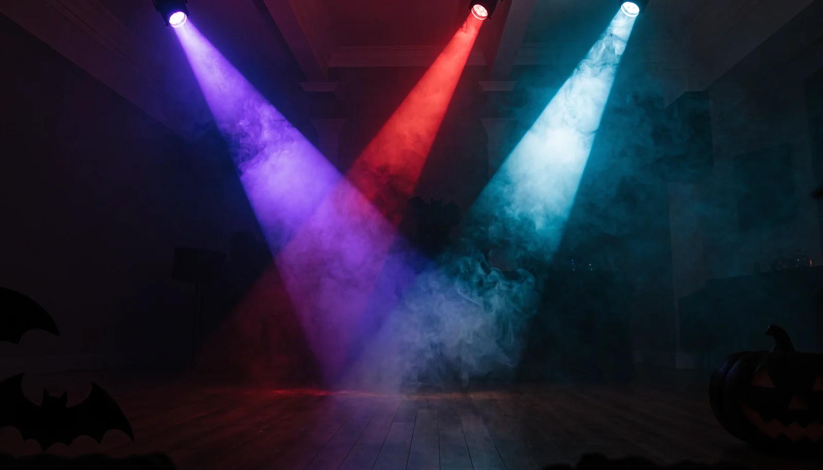 Drei farbige Lichtkegel stehen sichtbar im Nebel einer Halloween-Party
