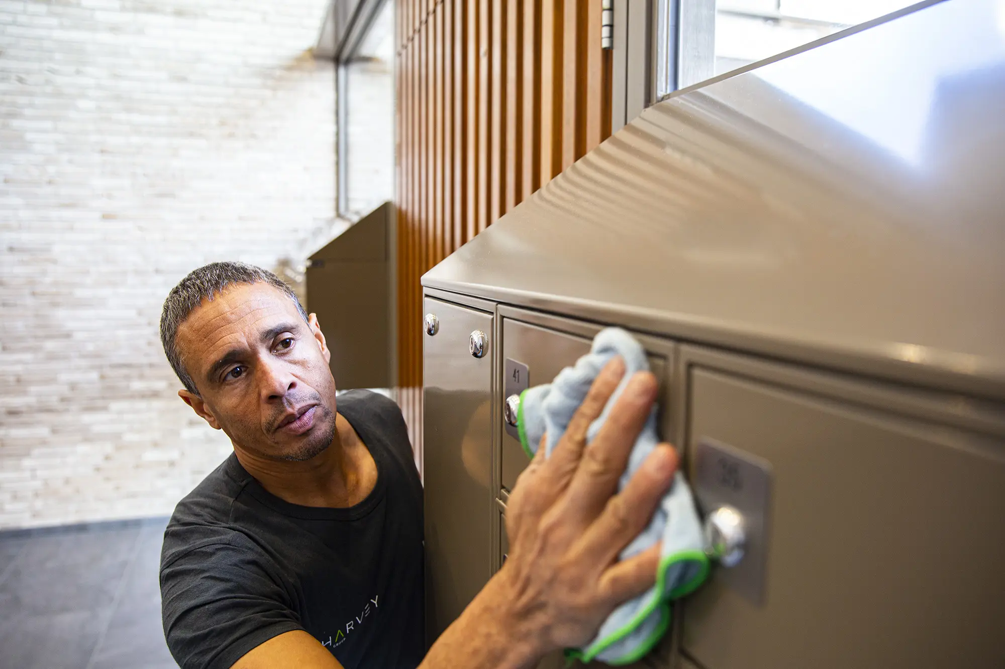 Man die een grijze postbox met een blauwe microvezeldoek schoonmaakt in een binnenruimte.