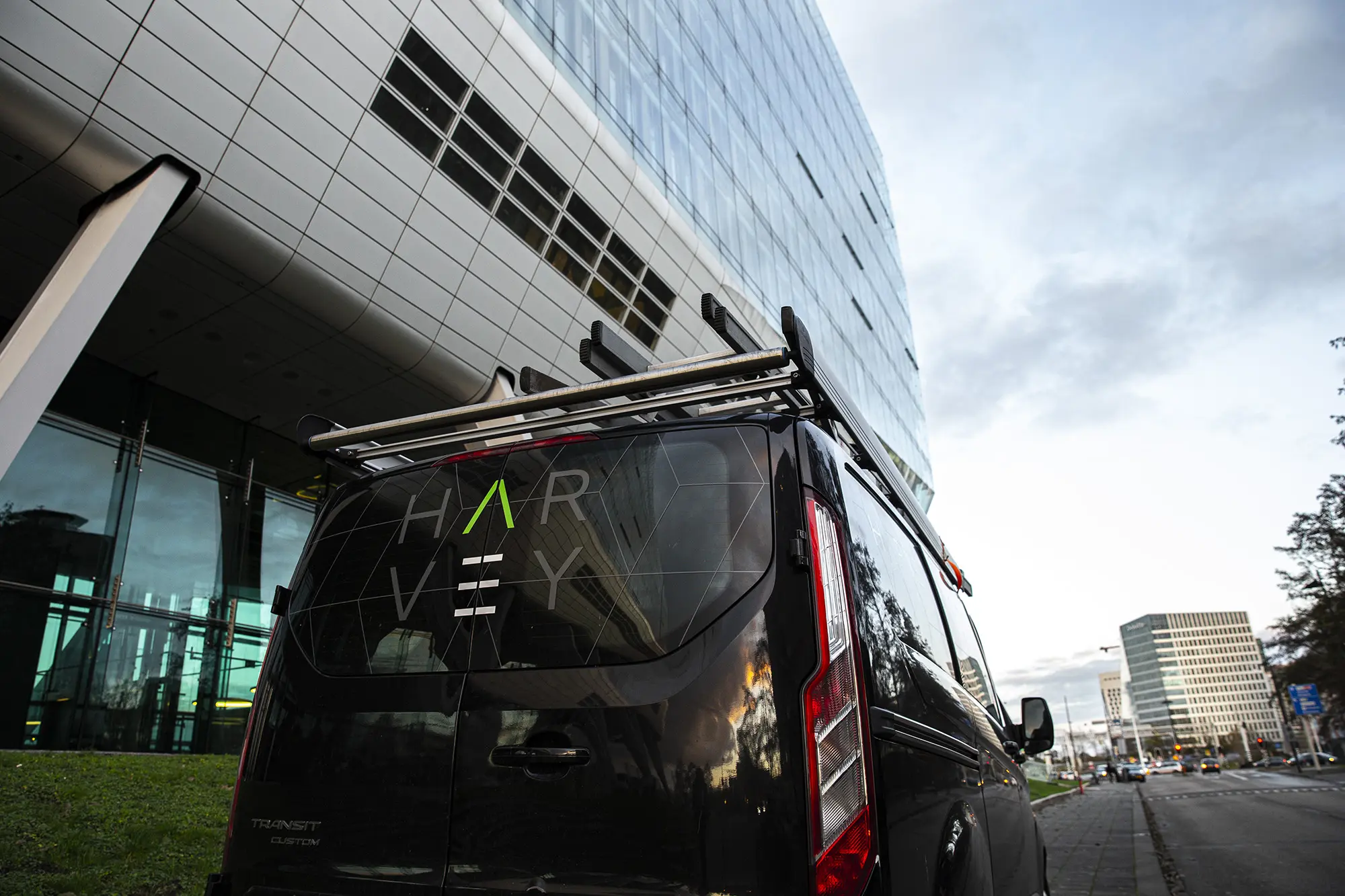 “Bestelbus van Harvey Facility geparkeerd bij een modern gebouw.”