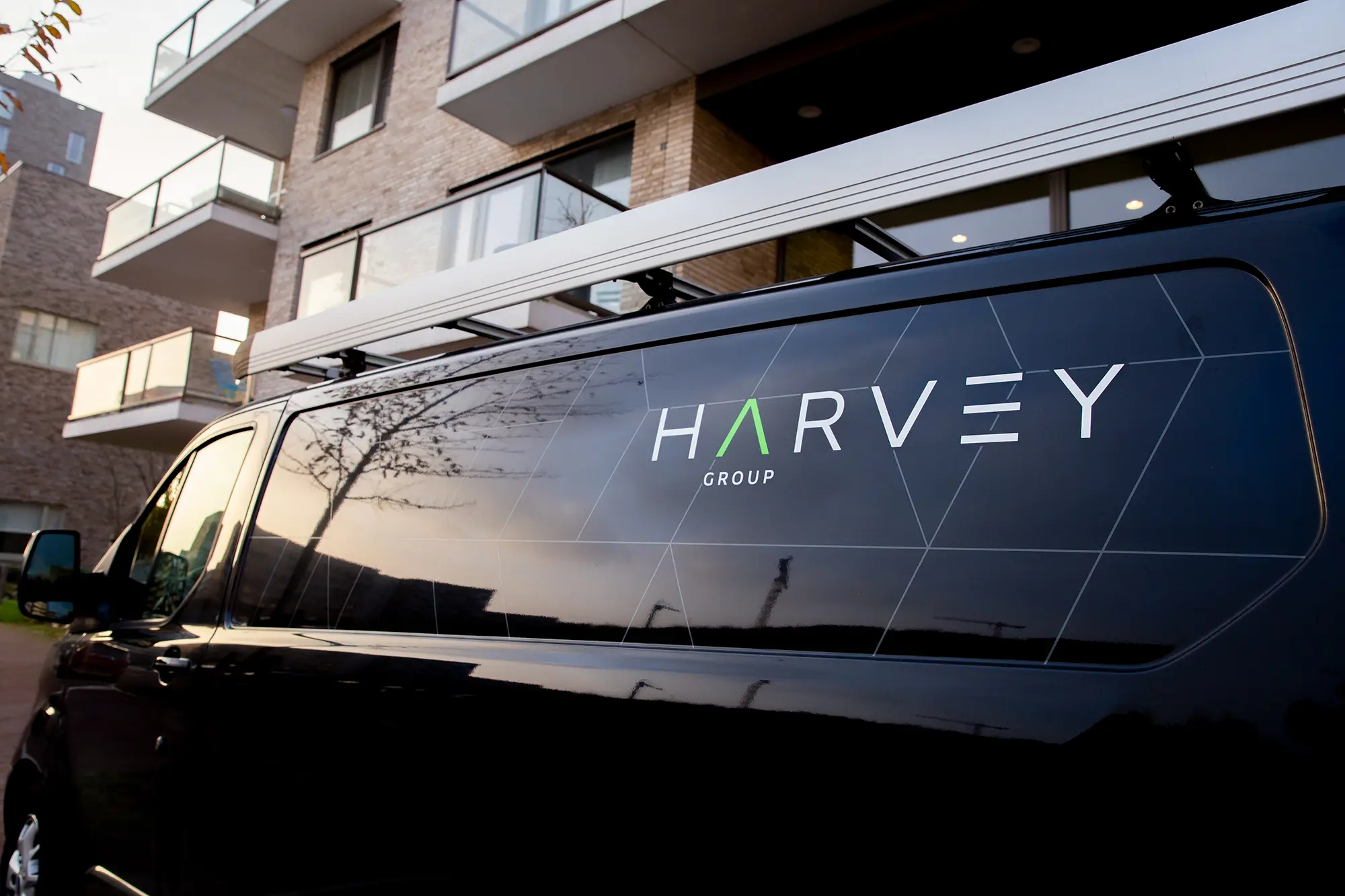 “Bestelbus van Harvey Facility geparkeerd bij een modern gebouw.”