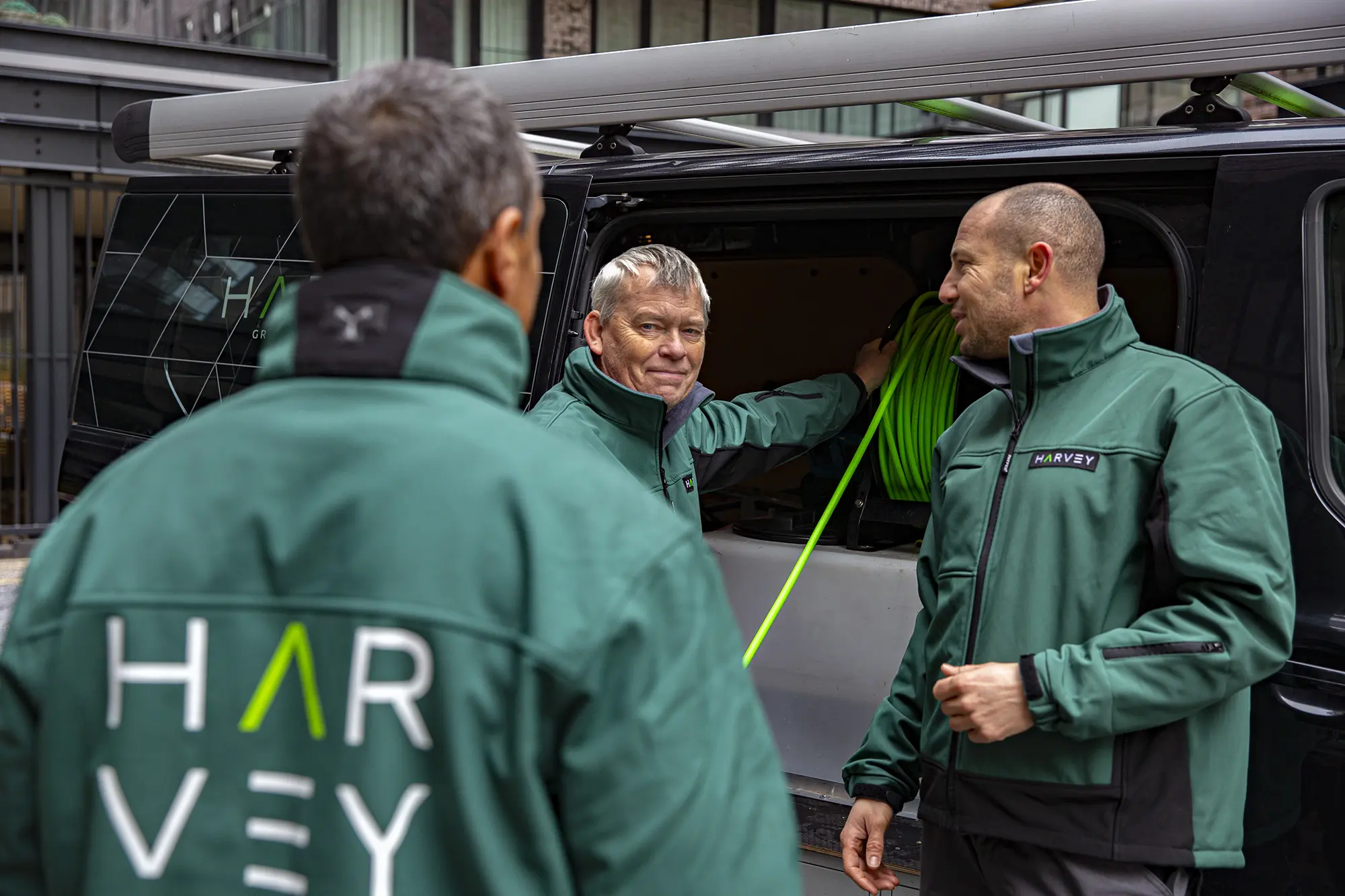 “Twee medewerkers van Harvey Facility in groene werkkleding die met elkaar overleggen bij een bedrijfsvoertuig.”