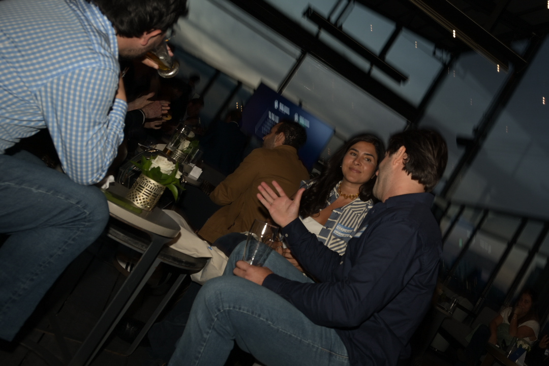 Attendees chat over drinks in a glass-walled lounge during an evening event