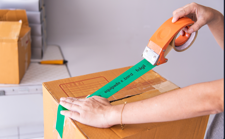 Hands sealing a box with green tape reading “equipado x .bord — frágil” (equipped by .bord, fragile)