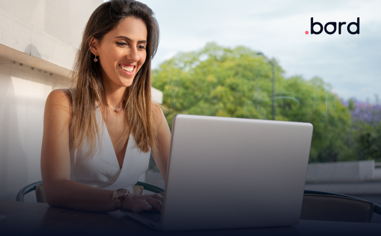 Smiling woman working on her laptop on a terrace with trees behind. .bord logo