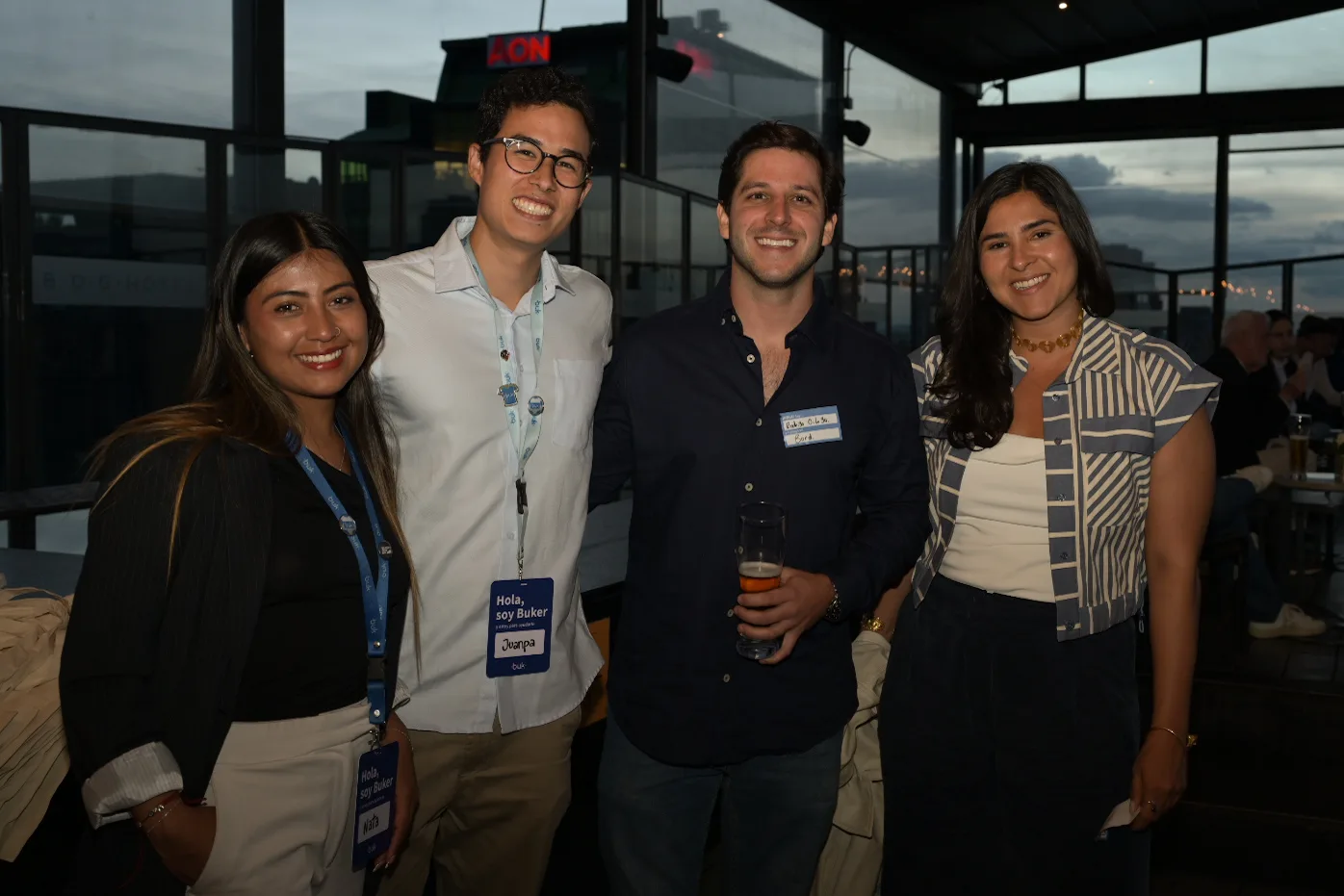 Four attendees smile with badges on an event rooftop at dusk; one wears a Bord name tag
