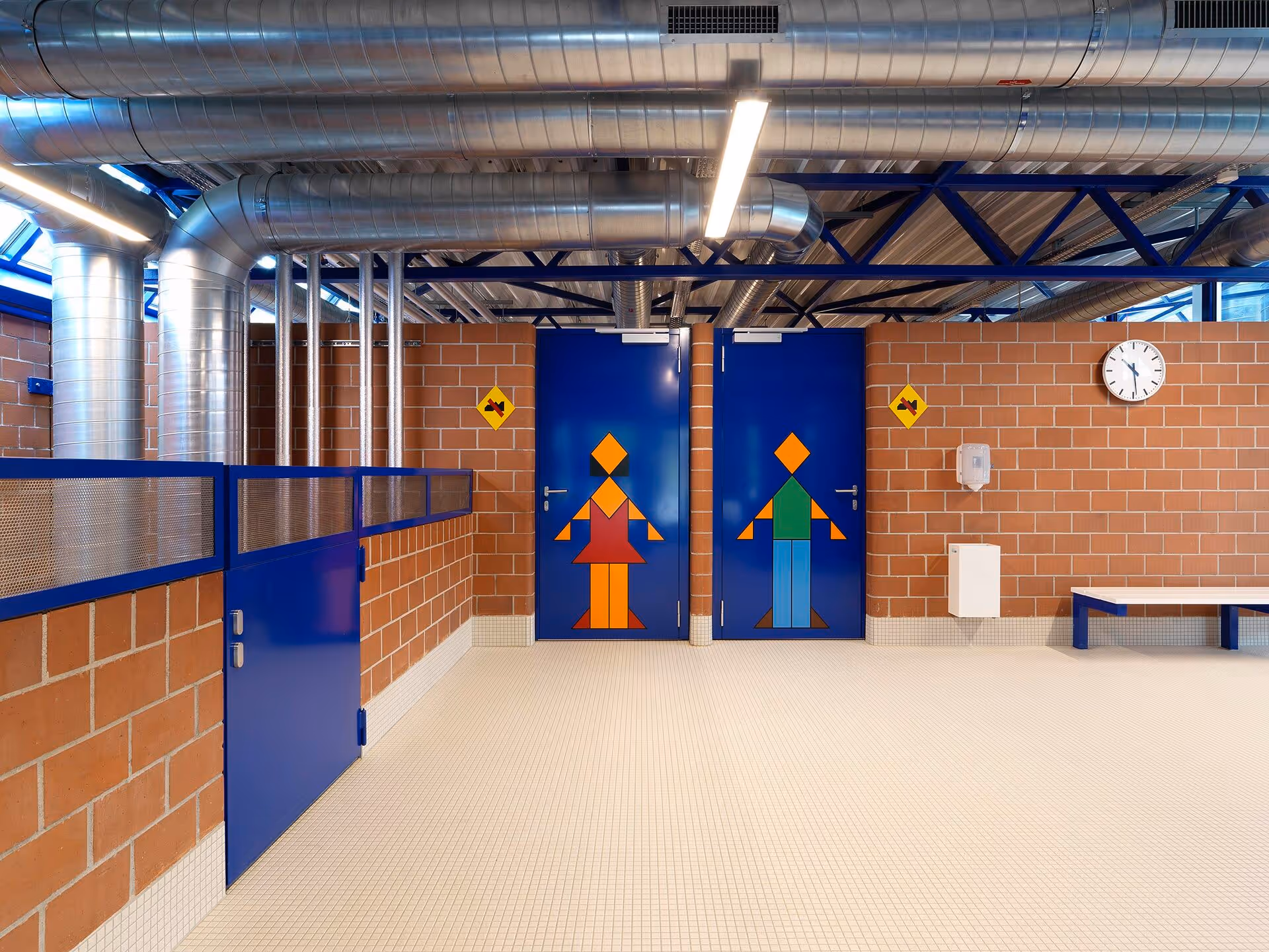 Industrial-style restroom entrance with blue doors featuring colorful geometric figures indicating female and male bathrooms.