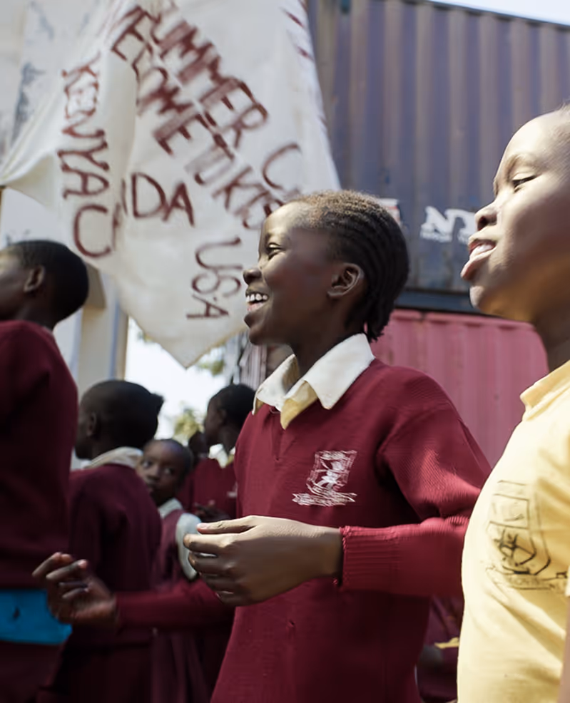 Group of smiling school children in uniforms standing outside near a painted banner.