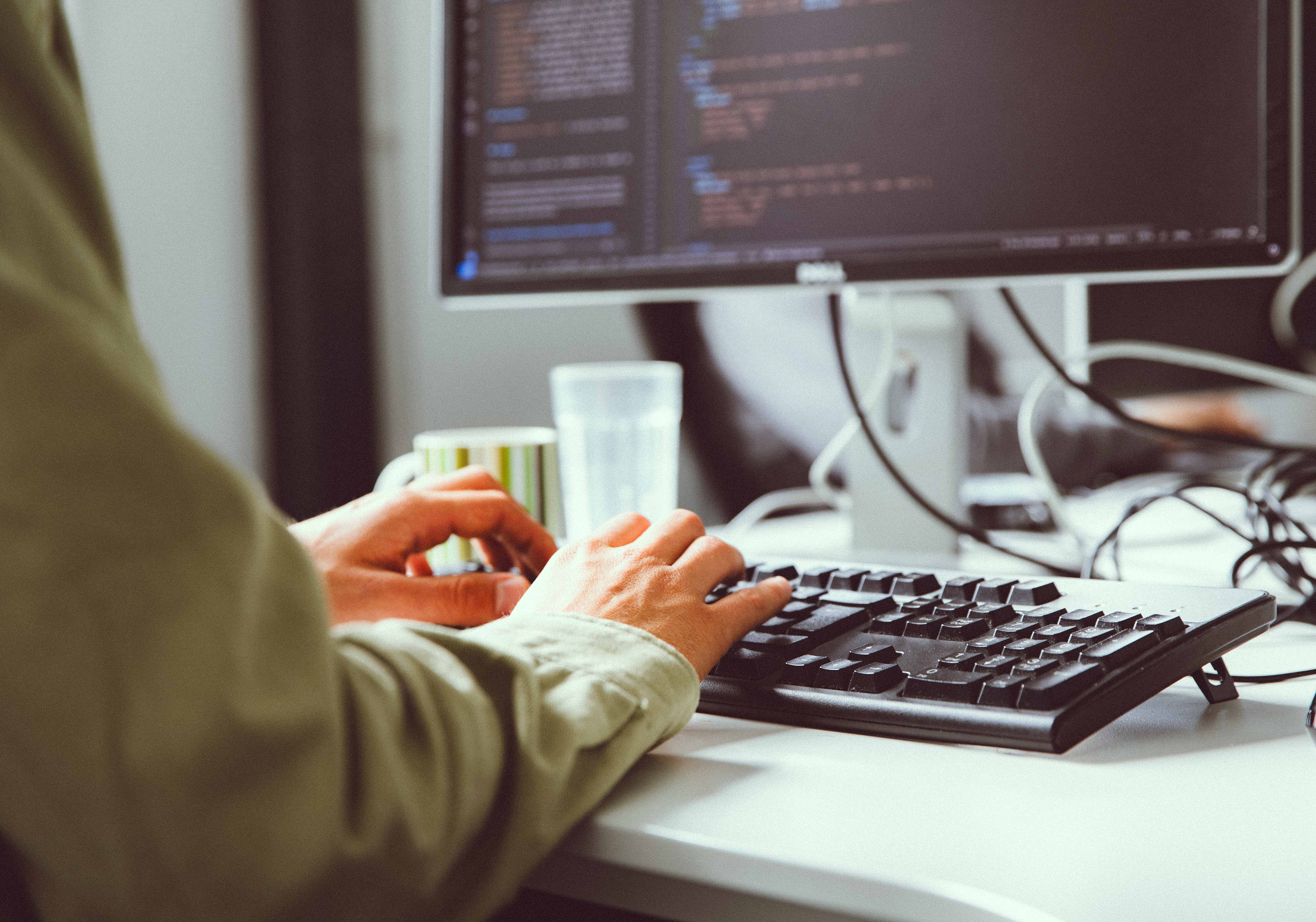 Person typing on a keyboard with programming code displayed on a computer monitor.