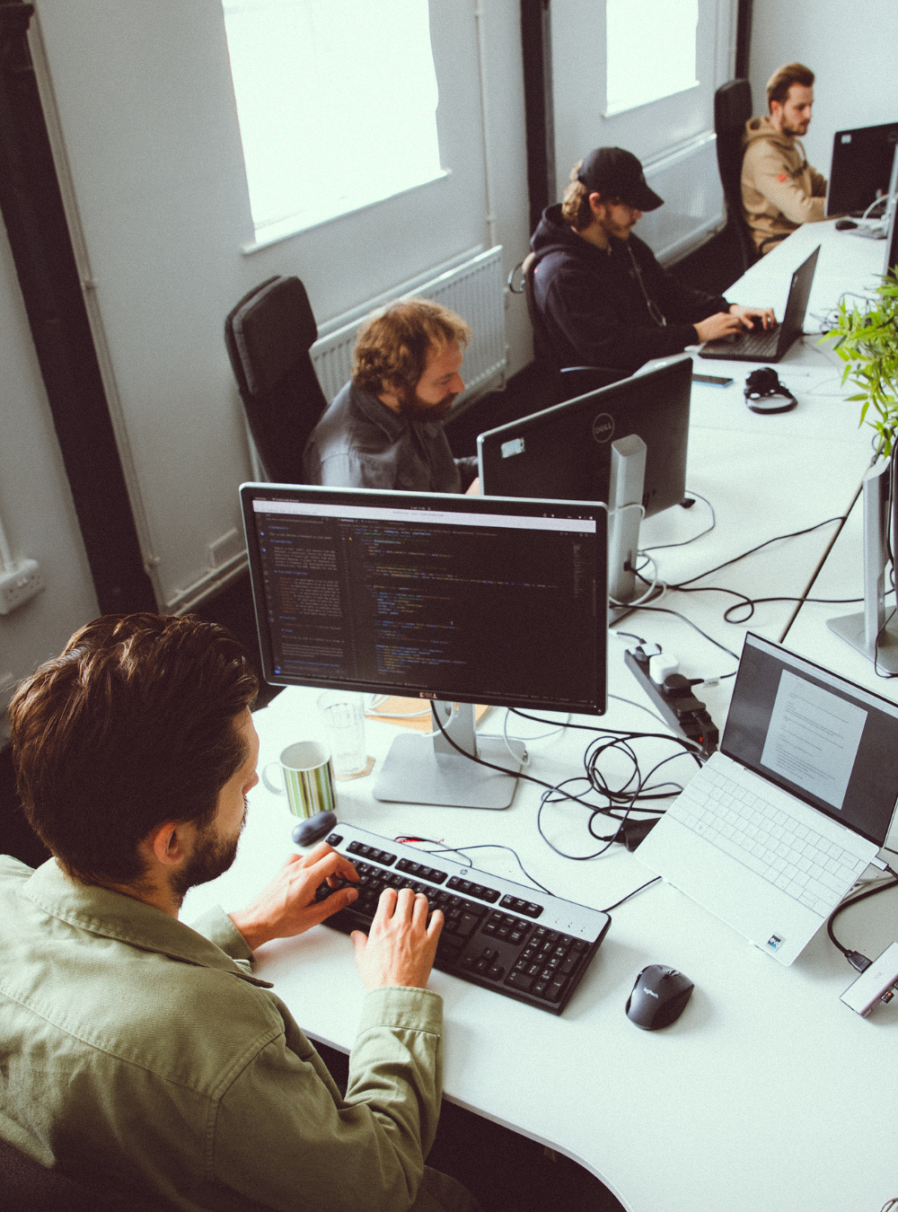 Man in a green checkered shirt reviewing papers with a pen in a dimly lit room with a blurred screen in the background.