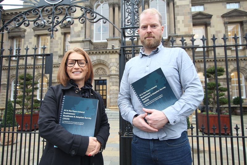 Lisa Comerton on the left and Martin Naughton outside Custom House in Belfast, holding AI Survey 2025 reports.
