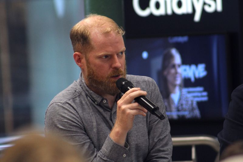 Martin Naughton speaking into a handheld microphone at the Catalyst AI panel.