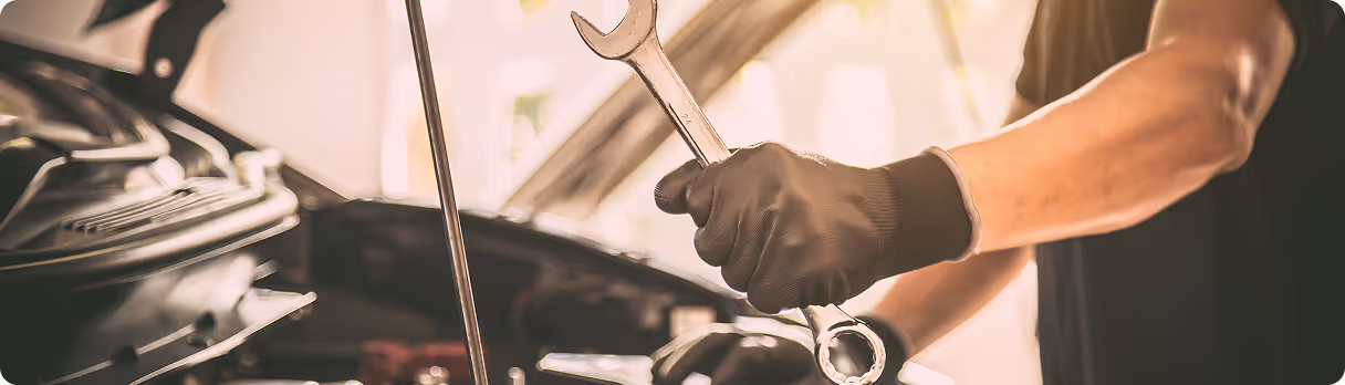 Mechanic wearing black gloves holding a wrench while working on a car engine with the hood open.
