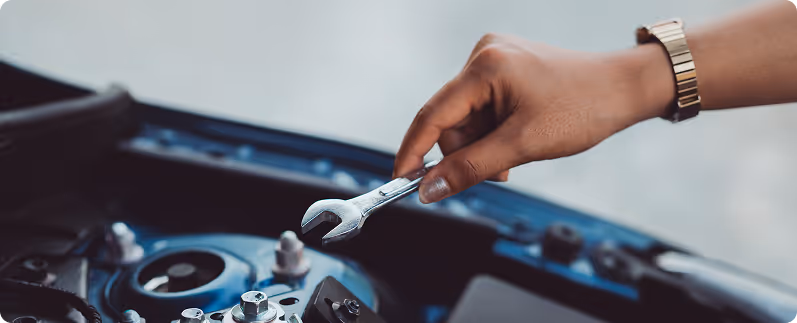 Person's hand holding a wrench repairing a car engine.