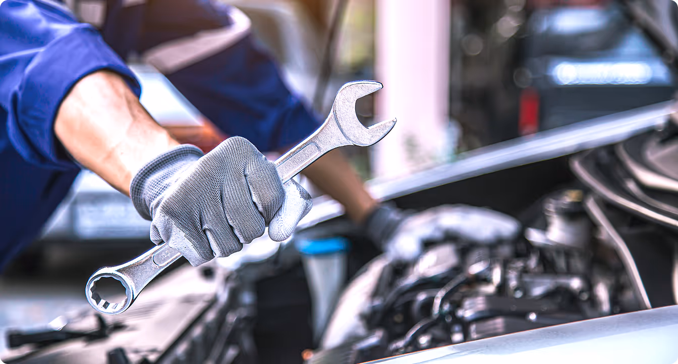 Mechanic wearing gloves holding a wrench while working on a car engine.