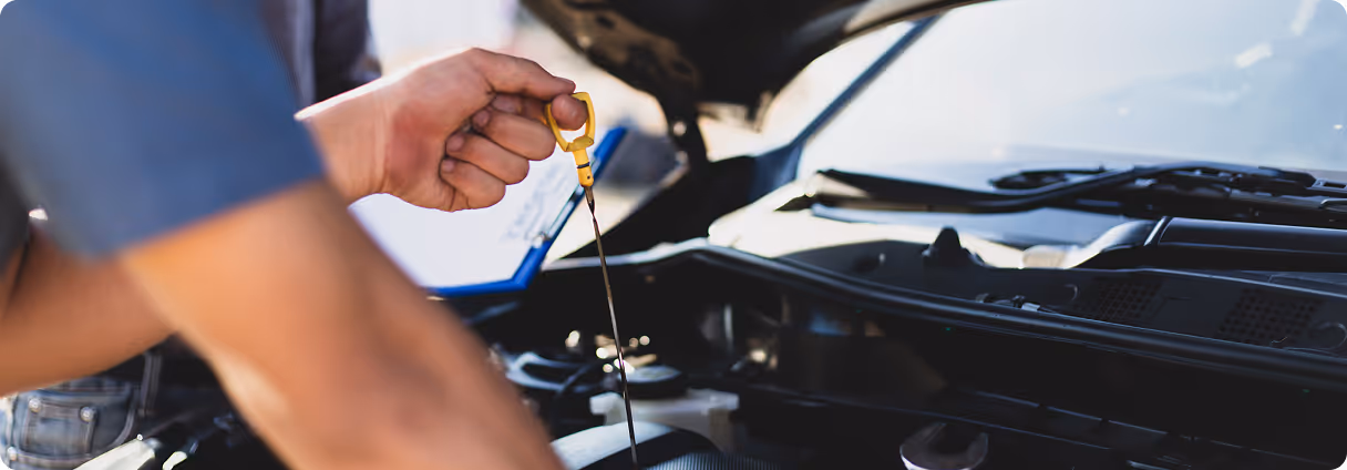Person checking engine oil level with a dipstick under a raised car hood.