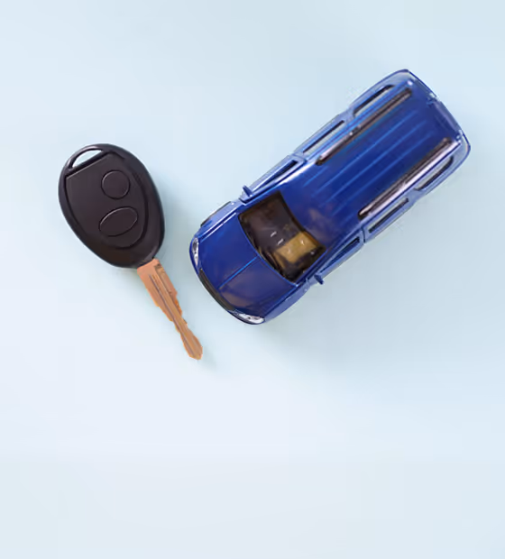 Black car key with remote and blue toy SUV on a light background.