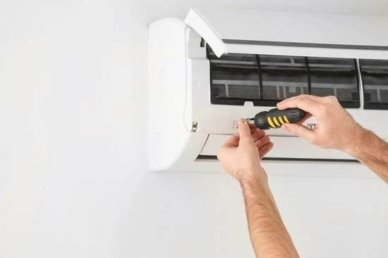 Man servicing wall-mounted air conditioner unit.