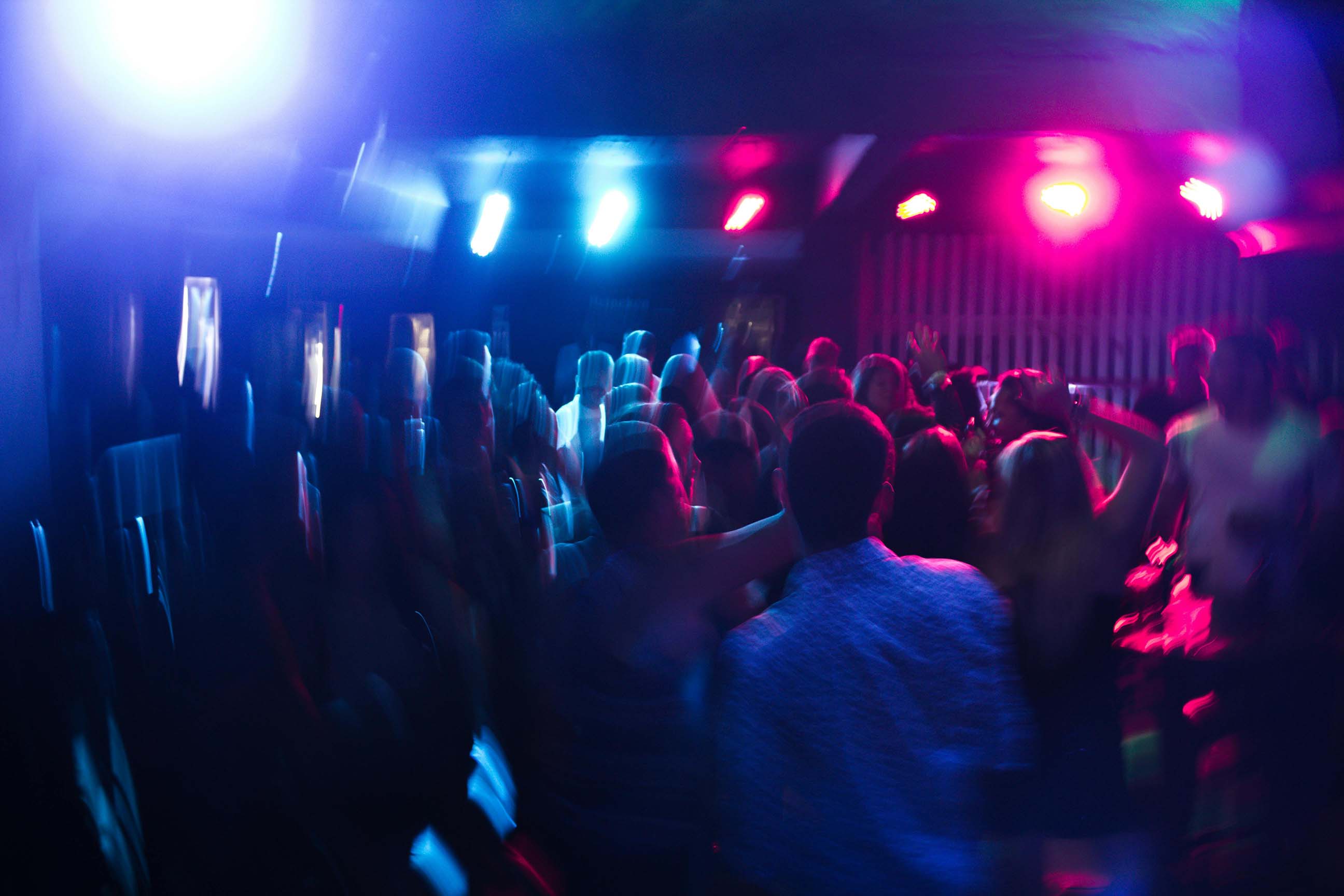 Blurred crowd dancing under colorful blue and pink club lights.