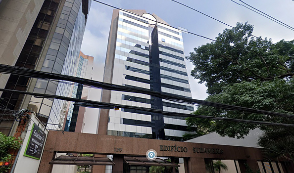 Tall modern office building with reflective windows behind an entrance labeled 'Edificio Sudameris' and nearby large trees.
